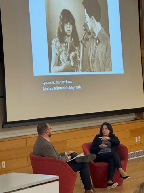Olga Fert in dialogue with Adam Moore. Projected on the screen behind them is an image of Fert’s daughter, Julia, and son, Alexander.
