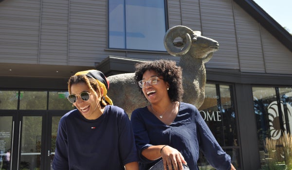 two students smiling in front of a URI ram statue