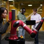 A team of students works with a robotic arm