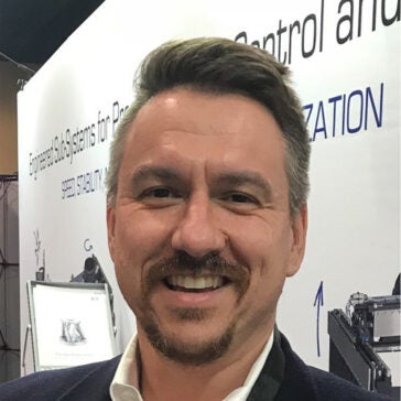 A headshot of David Rego wearing a dark suit in front of a banner at an engineering convention.