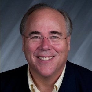 A head shot of Gary Baker wearing a dark suit in front of a gray background