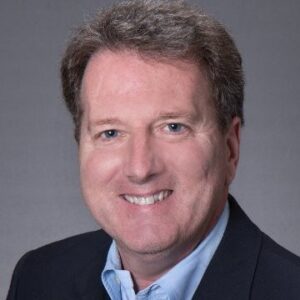 A headshot of Gary Spengler wearing a dark suit in front of a gray background.