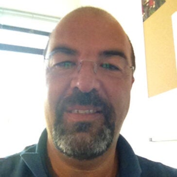 A headshot of Gianfranco Milani with glasses in a bright room.