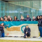 Hackathon coordinators pose in front of the engineering building with a Hackathon banner