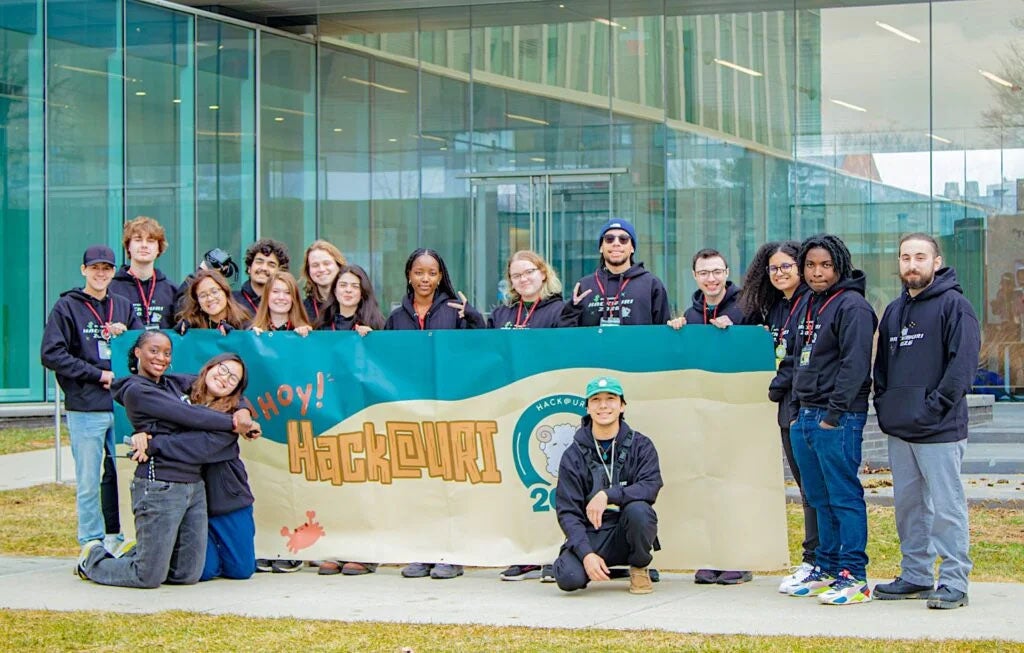 Hackathon coordinators pose in front of the engineering building with a Hackathon banner