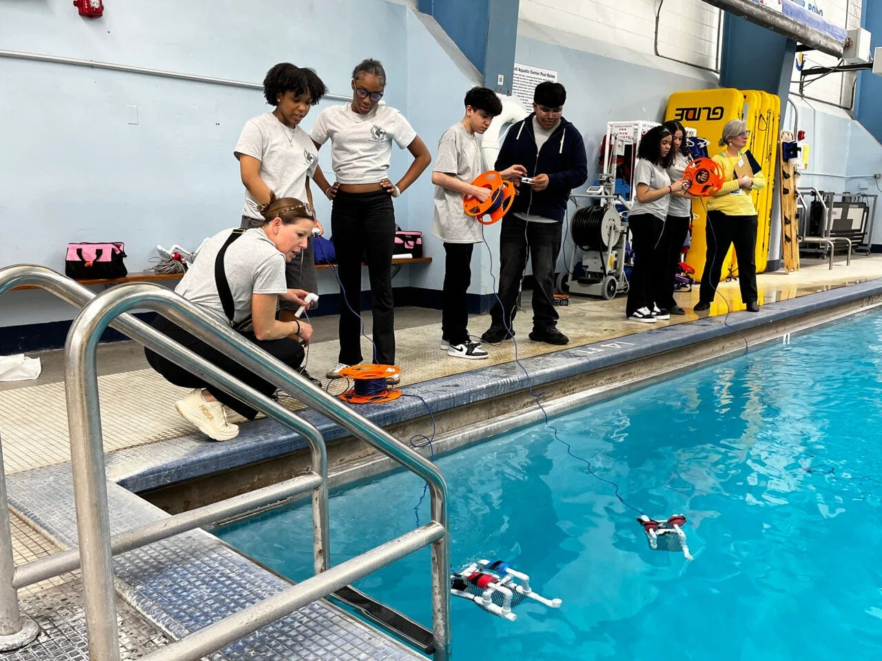 student stand outside a pool to watch robots perform in the water