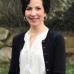 A formal portrait of Kristen Riley, posed in front of a landscaped background