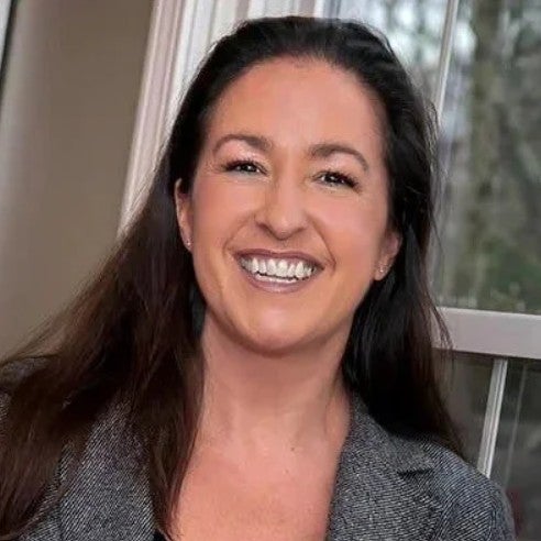 A professional headshot of Megan Echevarria wearing a gray blazer posed in front of a window