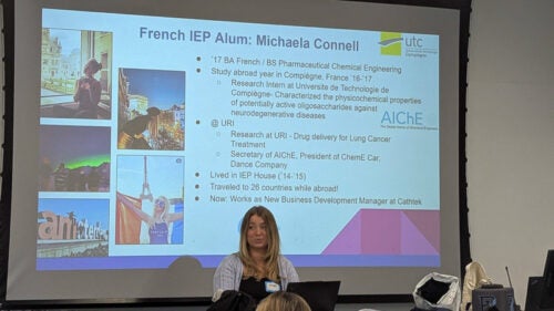 Michaela Connell stands in front of a slide that details her experiences in the French IEP and has several photos of her time in France.