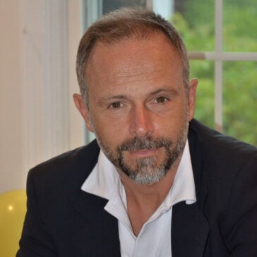 A headshot of Nicola Massarotti wearing a dark suit posed in front of a window.