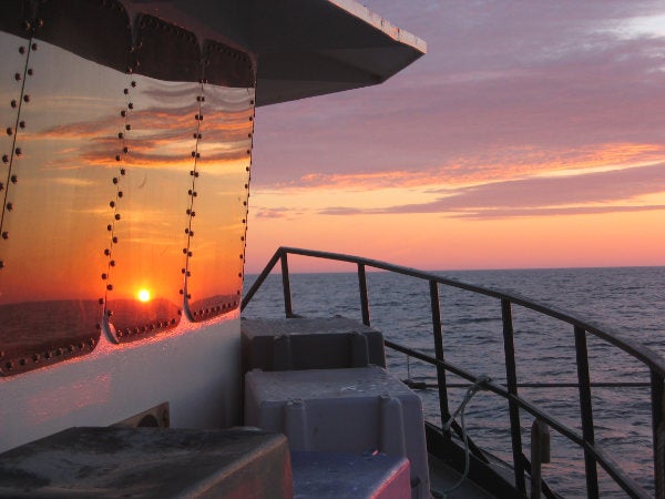A view of the sunset looking over the boat of a fishing vessel