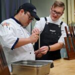 2 men in a kitchen cooking with knives in the side