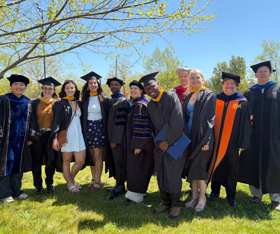 A group of graduates, their advisors, and the interim dean smile in their gowns.