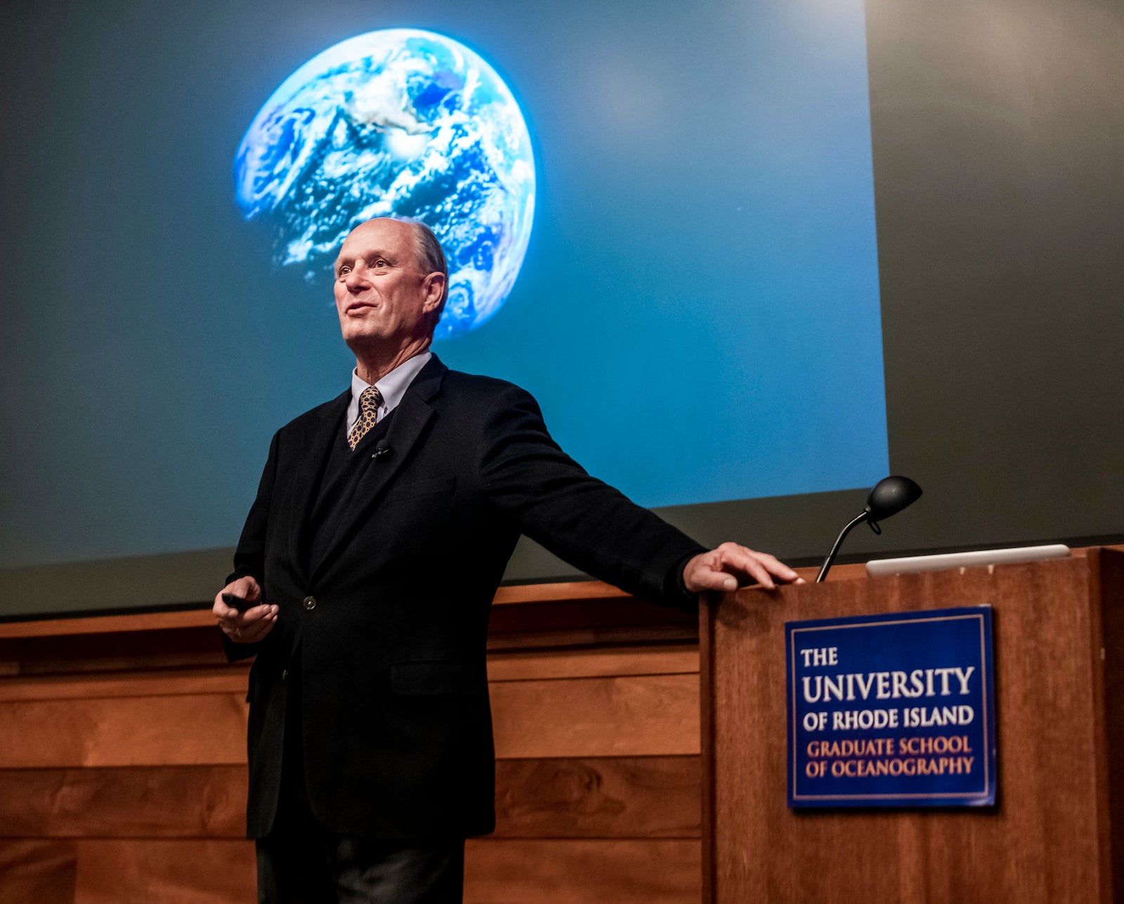 Robert Ballard standing next to a podium with an image of the Earth is projected on a screen behind him.