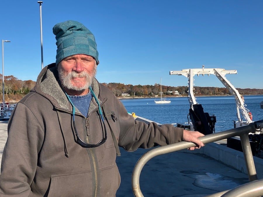Daniel Alexander facing the camera outside on a pier. He is wearing a hat and cool weather clothing. 