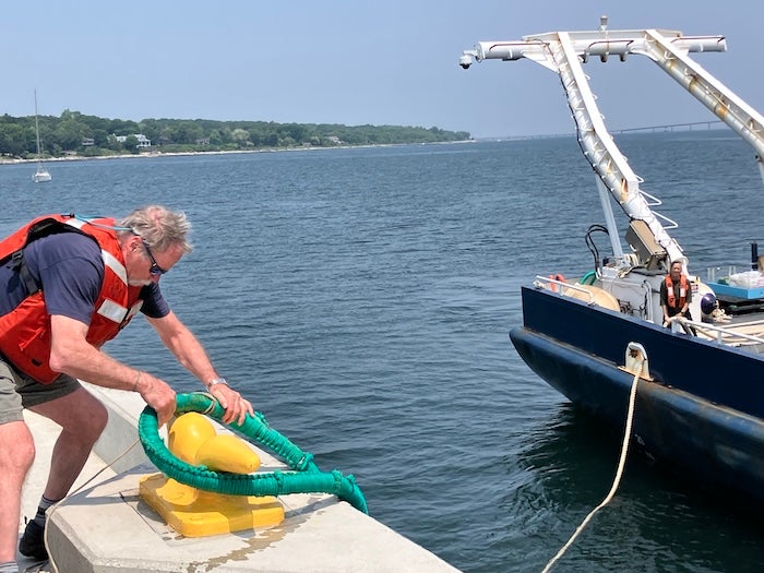 Dan Alexander on a pier during a sunny day. He is securing a large rope from the research vessel Endeavor to a cleat on the pier. 