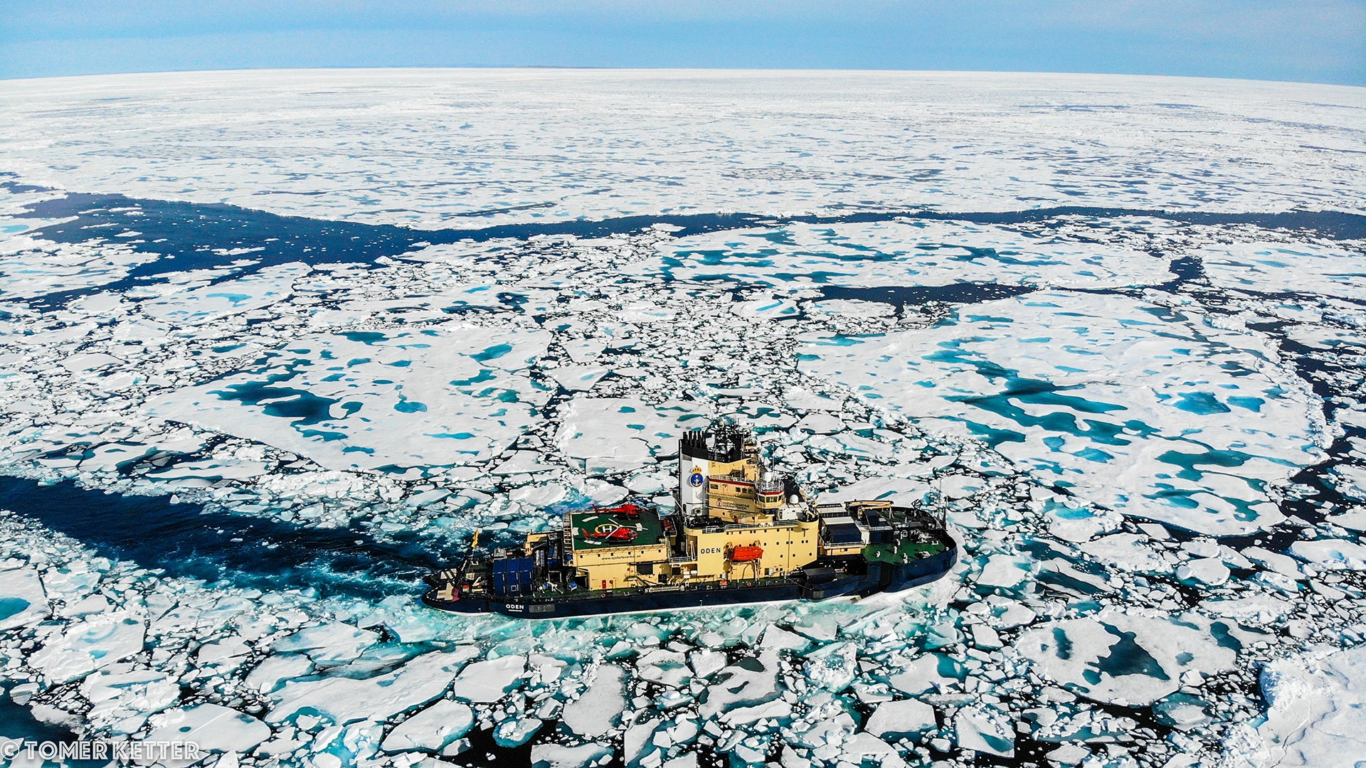 aerial photo of a black and yellow icebreaker vessel in the middle of an ice-covered sea.