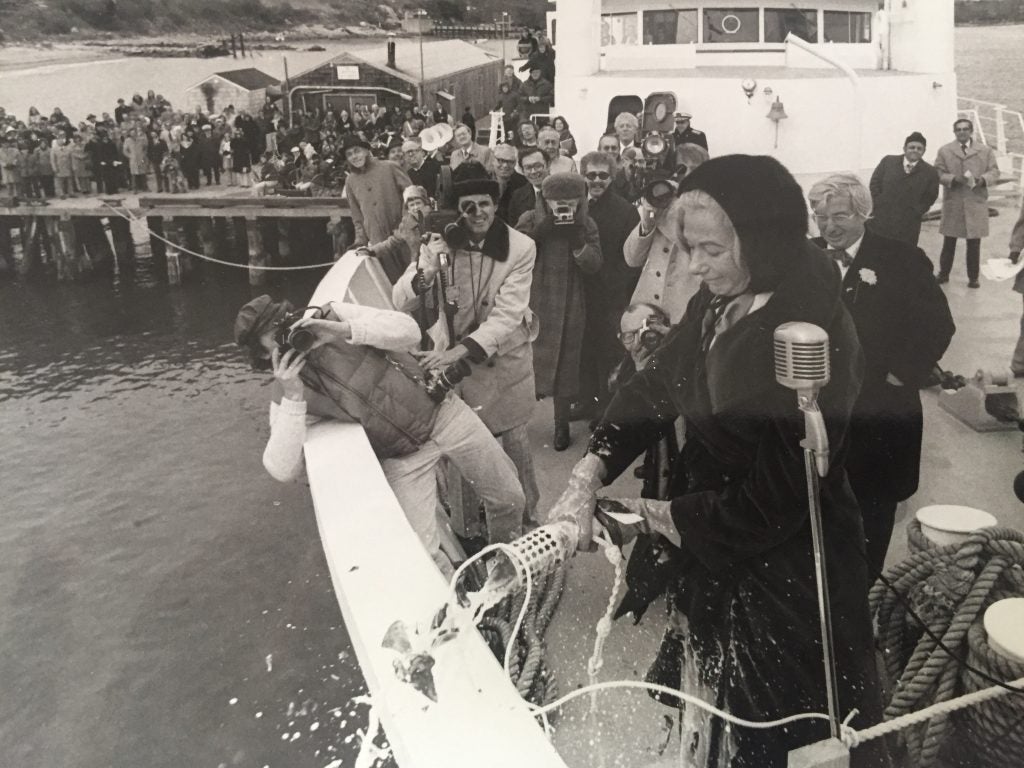 A woman christening R/V Endeavor with a bottle while a large audience looks on. 