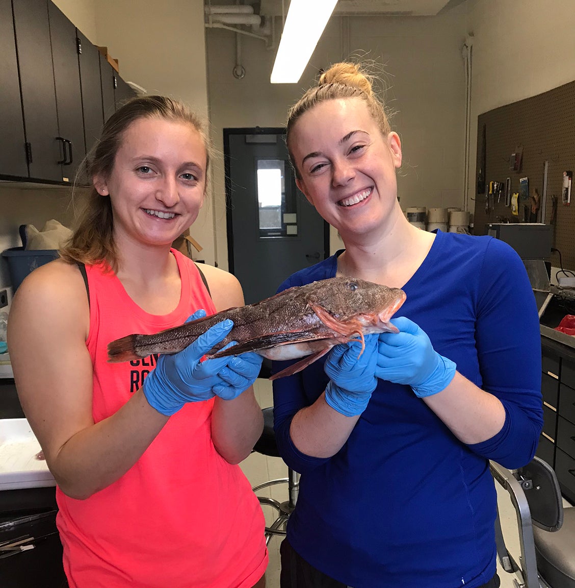Graduate students Annie Innes-Gold and Maggie Heinichen pose with a fish in a lab.