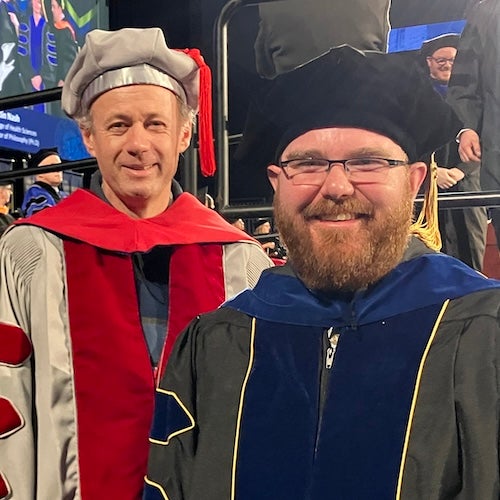 Sam Katz and Rainer Lohmann at a graduation ceremony, both wearing caps and gowns. 
