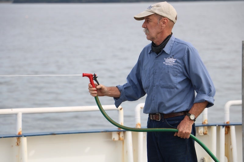 Kevin Walsh aboard a ship, outside on the deck, and cleaning the ship with a hose.