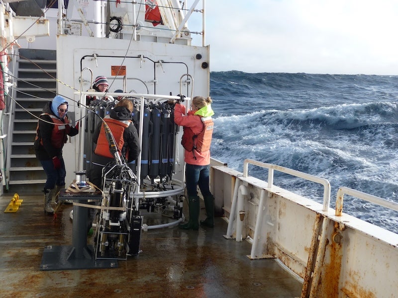 People on the deck of a ship in rough seas preparing a large scientific instrument. 