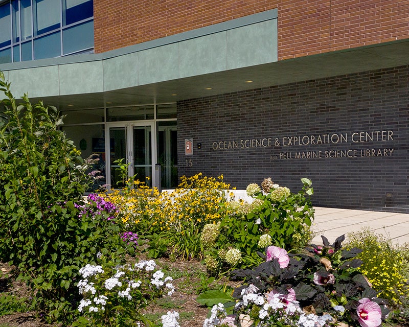 Entrance of an academic building, garden flowers in the foreground, and the building sign reads "Ocean Science and Exploration Center."