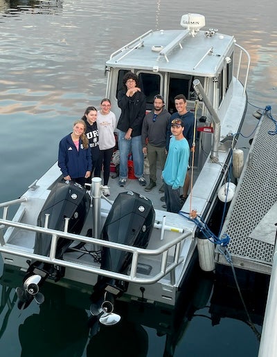 Seven people aboard a small research boat which is tied to a dock. 