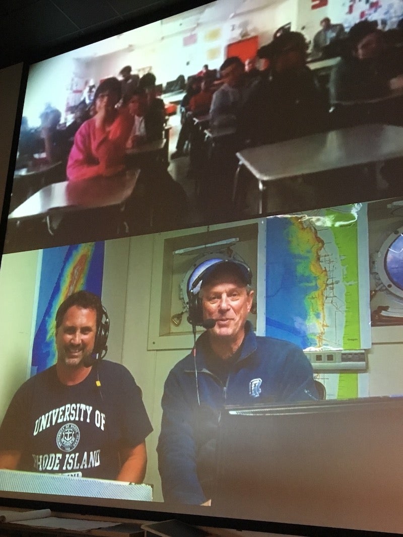 Two video screens showing scientists aboard the E/V Nautilus speaking with students at Central Falls High School.