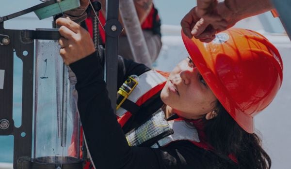 a marine professional works on a piece of equipment on a boat while wearing a hardhat