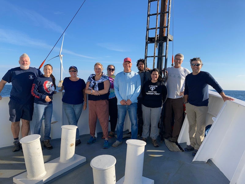 A group of educators on teh bow of a research vessel under clear skies.