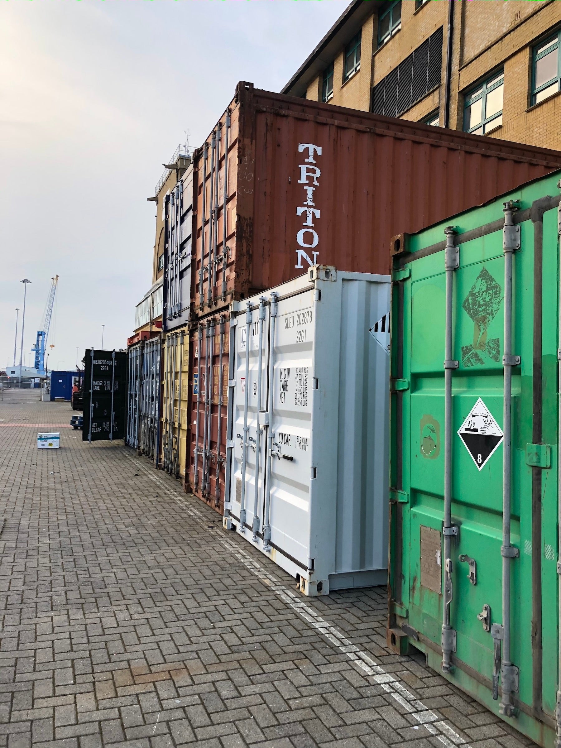 Several metal shipping containers on a pier; they are painted differnet colors: white, green, brown, yellow and blue.