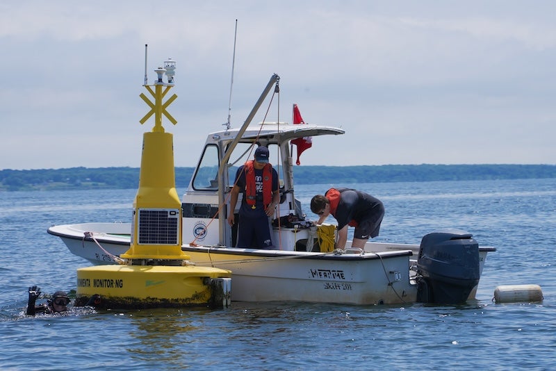 Two people aboard a 20-foot boat in calm coastal waters conducting research. 
