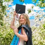 Photo of Ariana Temelini with her graduation cap and gown outside surrounded by flowers