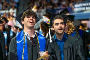 two graduating seniors smile together at graduation