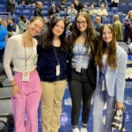 4 female sports media students posing for a photo at a URI game