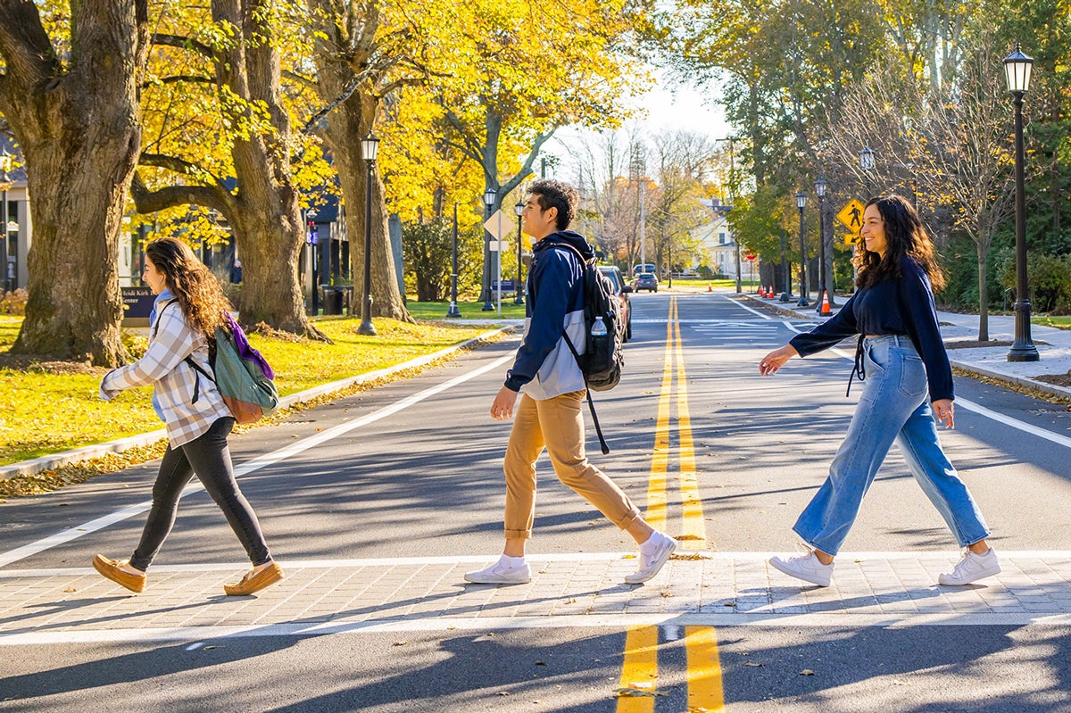 Three students walking across the road on campus