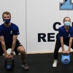 two students lifting kettle bells with face masks on