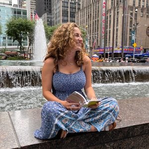 Tara reading a book on a founain in newyork looking right