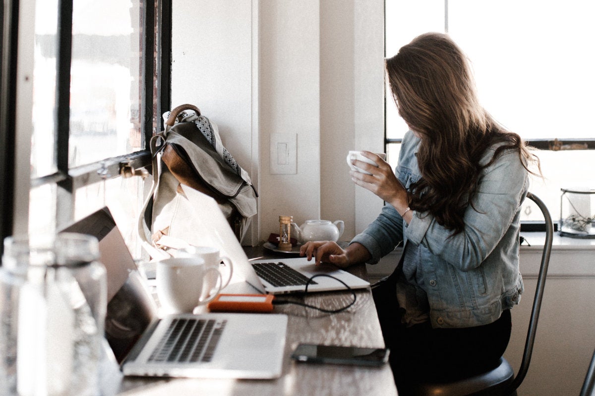 A person in a coffee shop with a backpack studying on a computer.