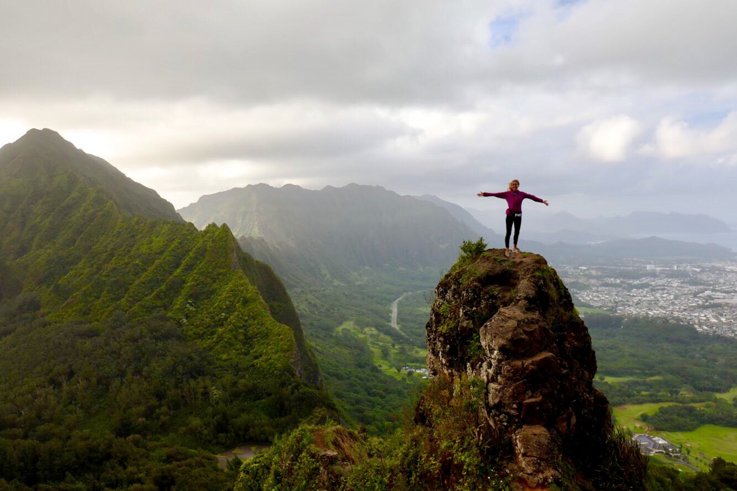 Morgan Gilman standing on a rocky promontory over a small urban landscape in Hawaii