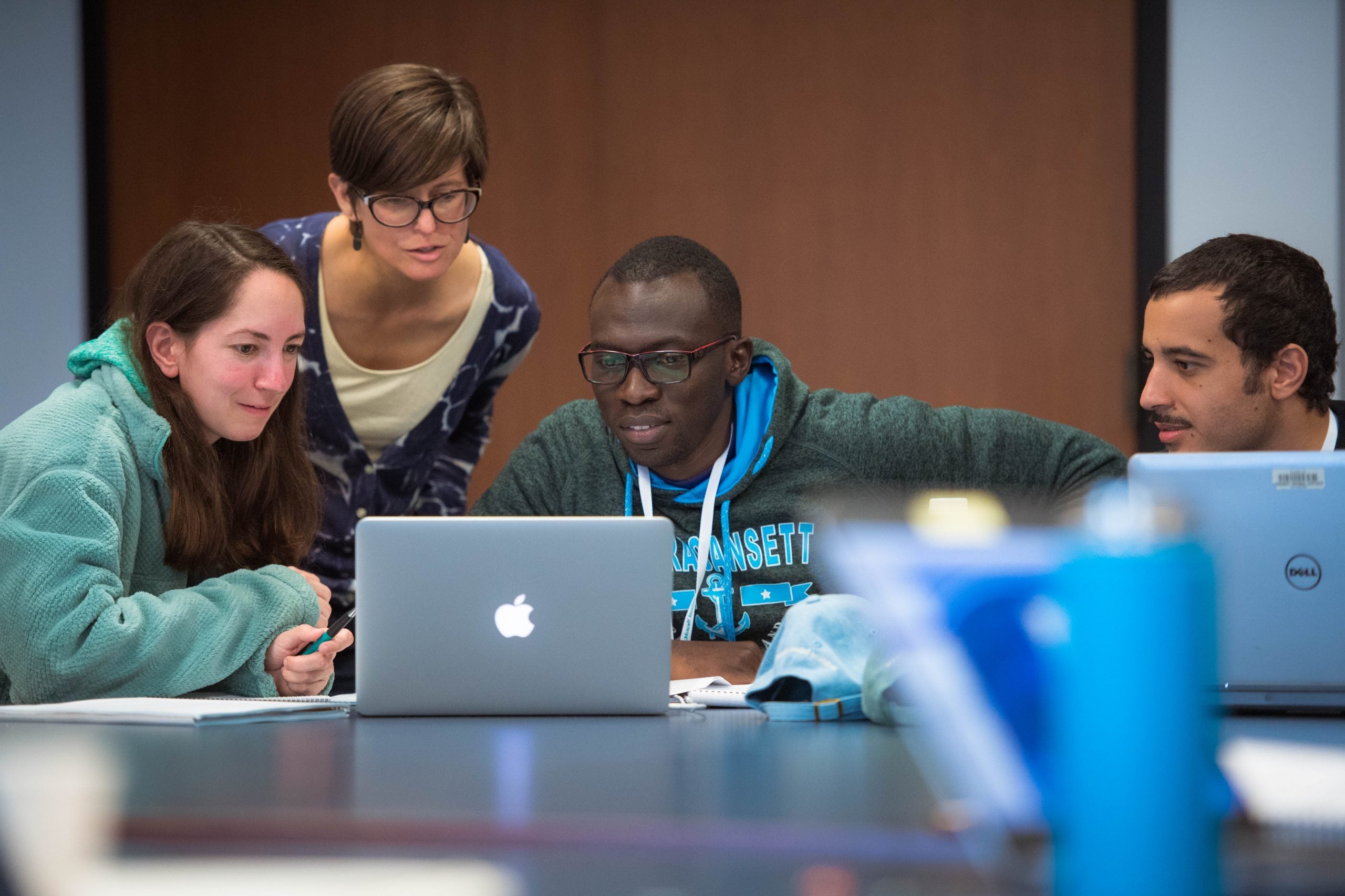 Photo of four people sitting at a conference table, smiling as they look at a computer screen.