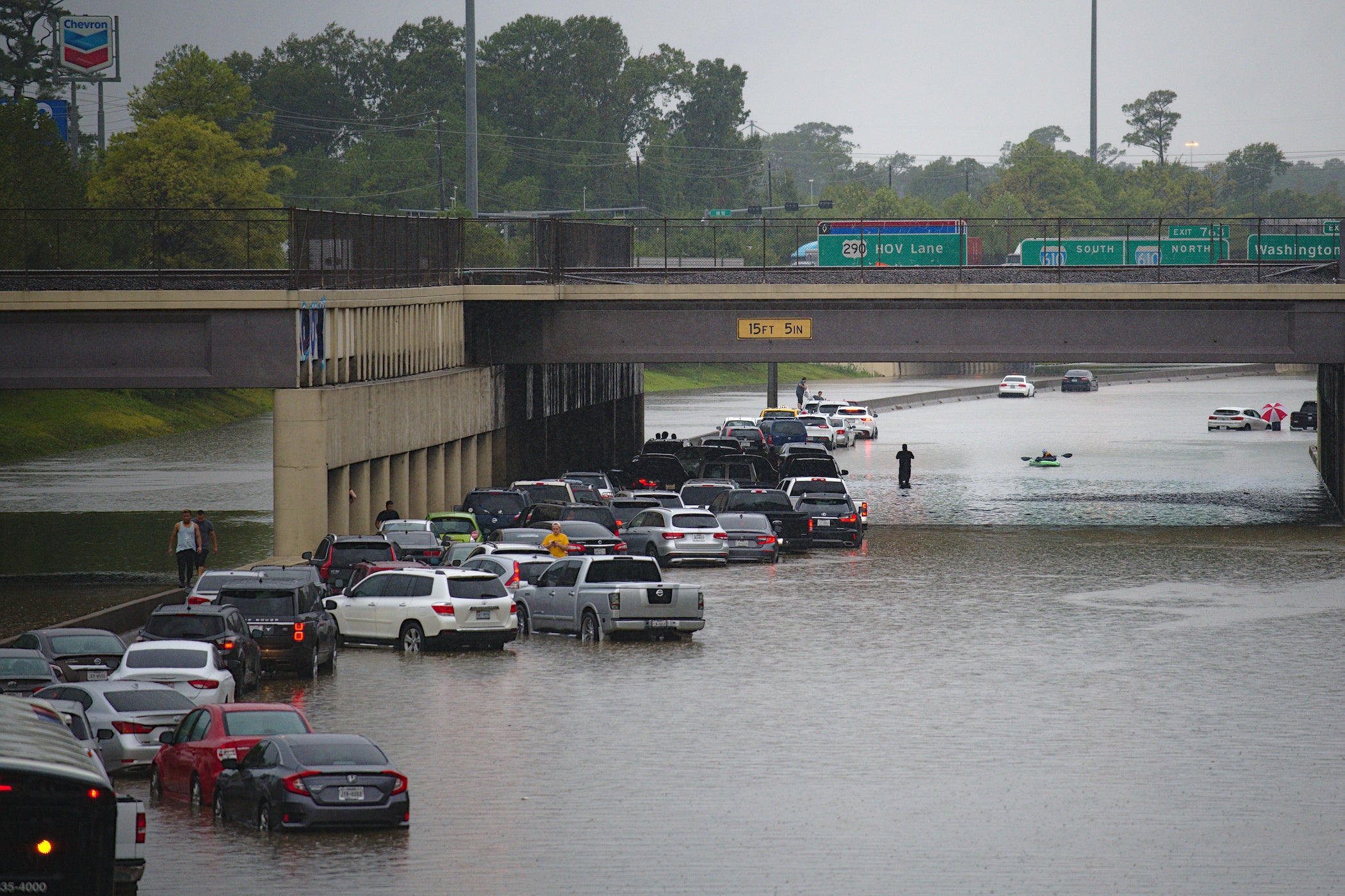 Photograph of many cars trying to drive through flooded area under a bridge.