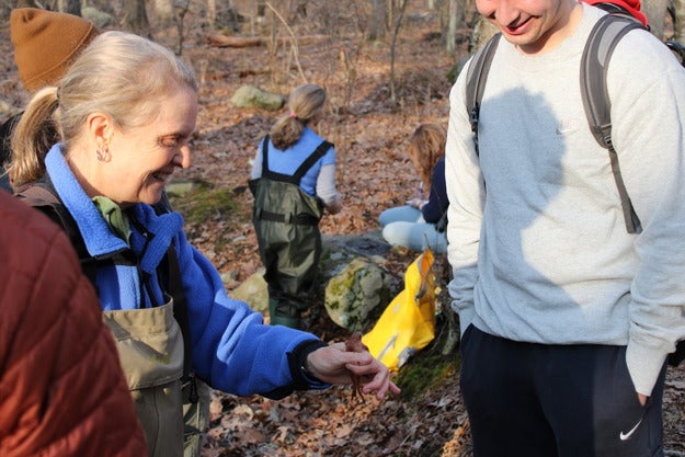 A smiling professor holds out a frog to a student.