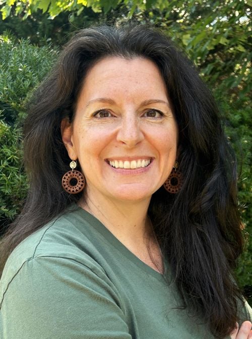 Erin Edmonds, wearing a green shirt and smiling with green bushes in the background.