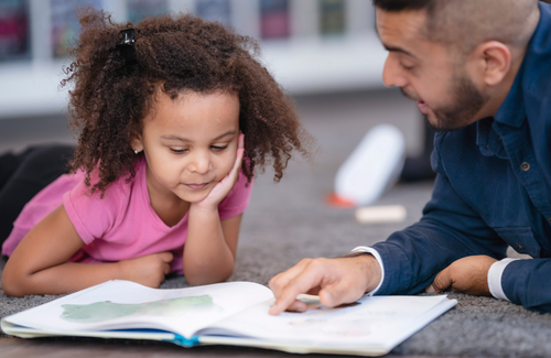 A male teacher helps a kindergarten student read a book