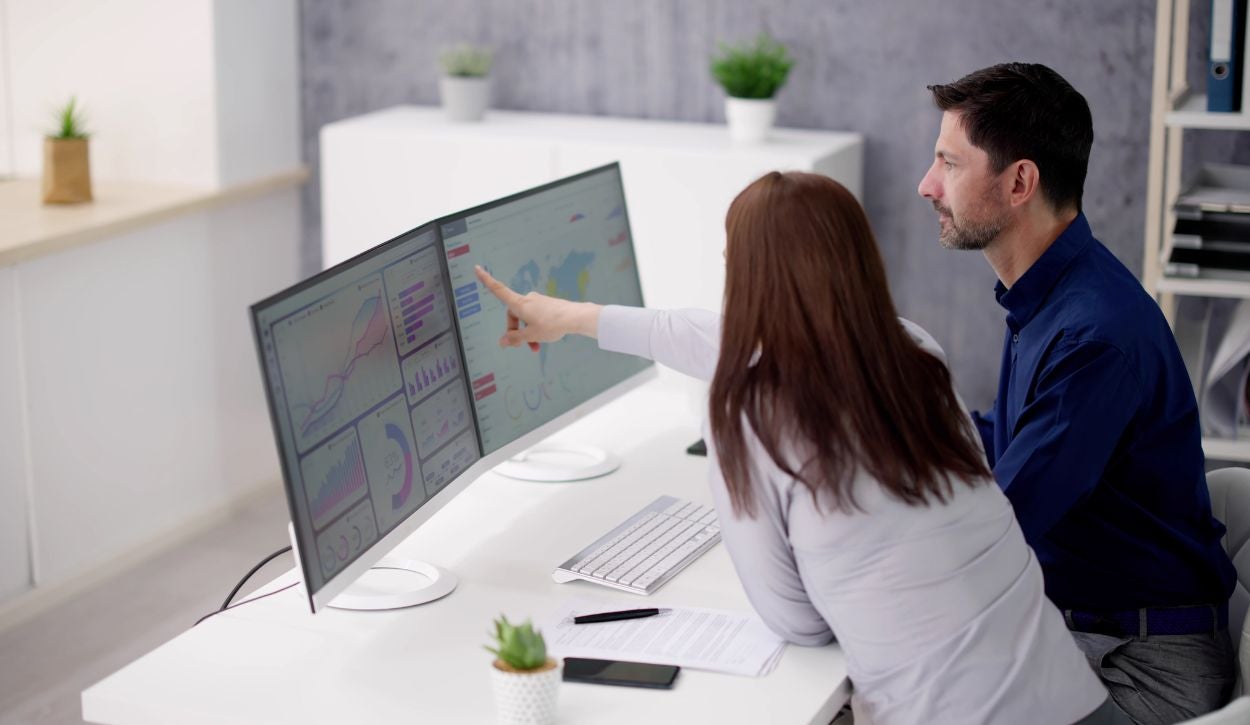 Two data analysts look at a map on a desktop computer.
