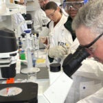 A group of people wearing laboratory gear, from the BioPharma course offered by PDI