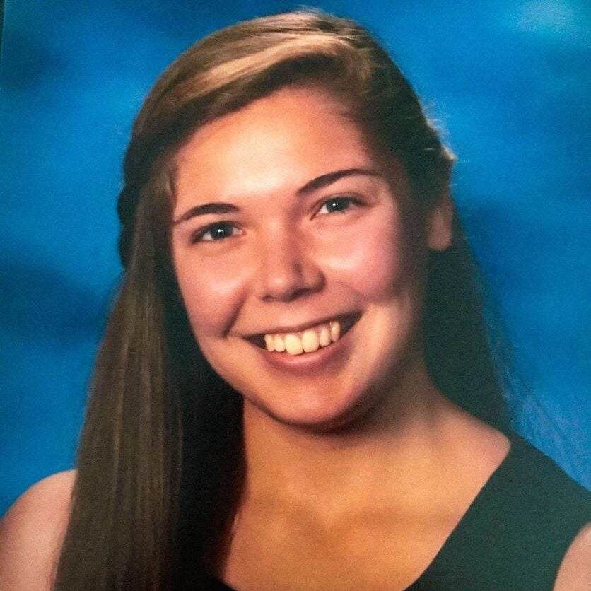 Sarah headshot- woman in black shirt in front of blue background.