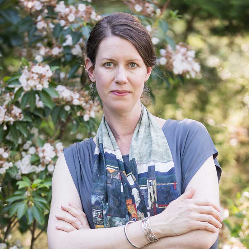 Lisa headshot- woman in blue shirt standing in front of flowers.